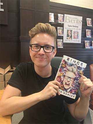 Tyler Oakley proudly holding his new book, Binge